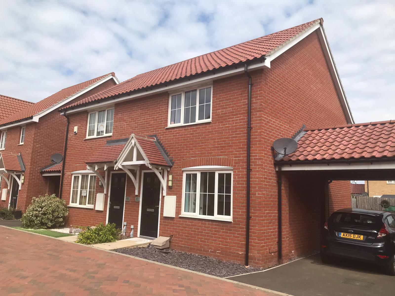 House on a street with a garage next to it. Fiesta car parked inside. cloudy sky