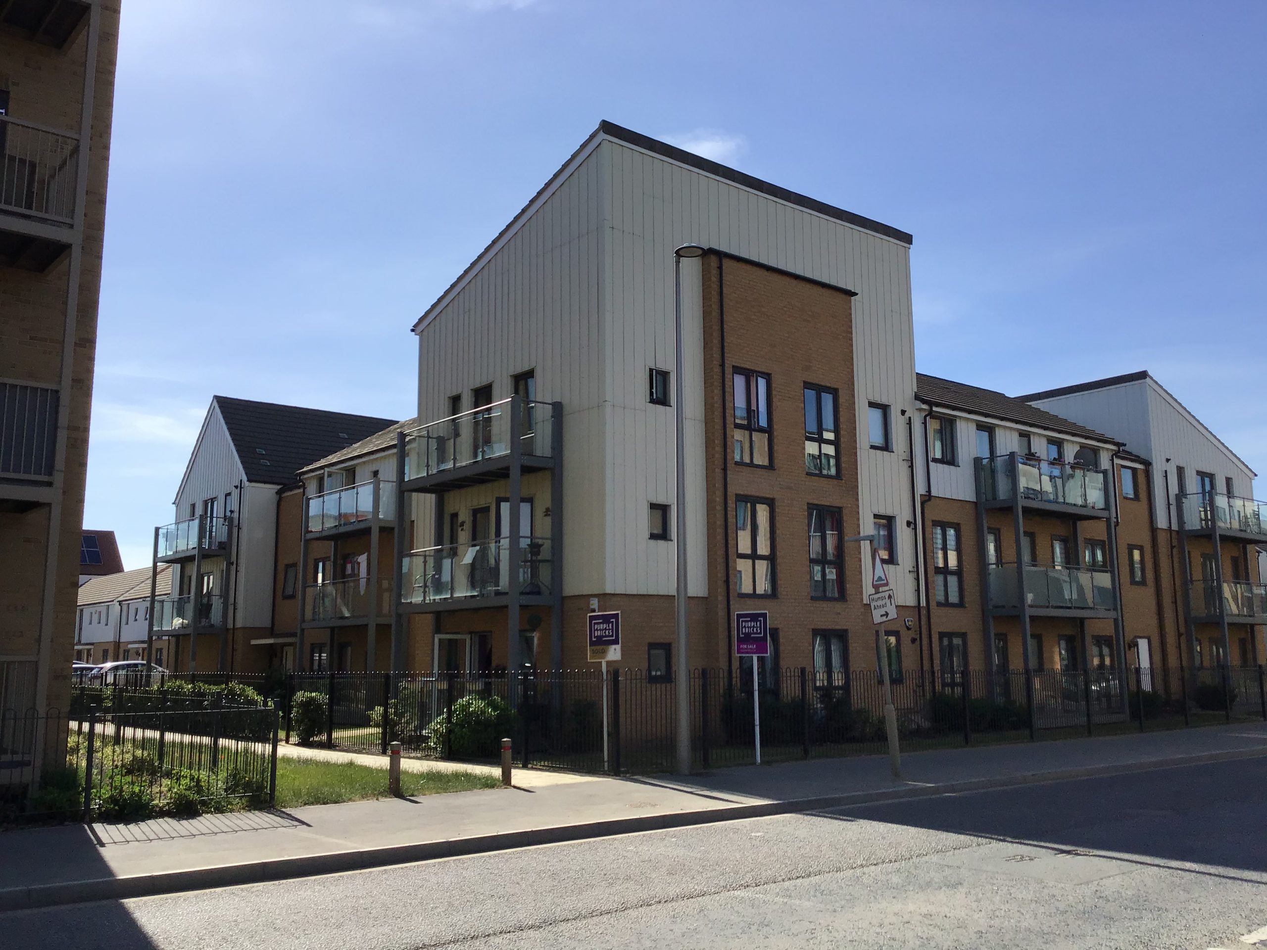 3 story block os flats with balcony's. some have for sale signs. front shared green / garden space. bright blue sky.