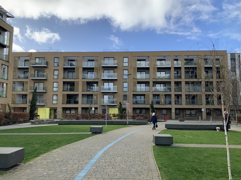 5 story block of flats all with large sliding doors and balcony's with communal garden. woman walking a dog in garden
