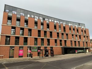 5 story commercial building and flats / apartments. Bus stop on the road. Grey sky.