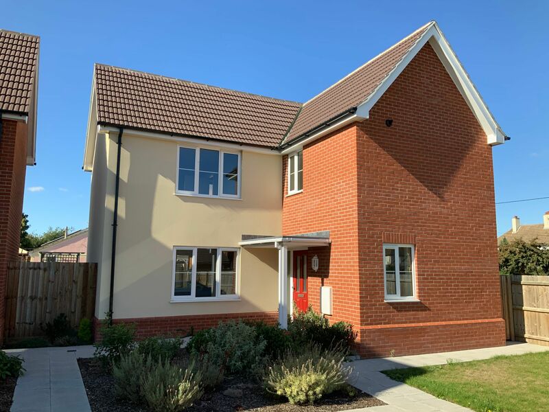 L shaped brick house with red door and landscaped driveway and front garden. blue suny sky.